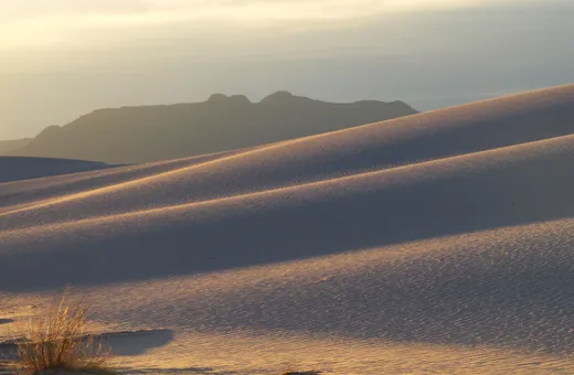 Early sunlight tracing white sand dunes with a mountain range on the horizon